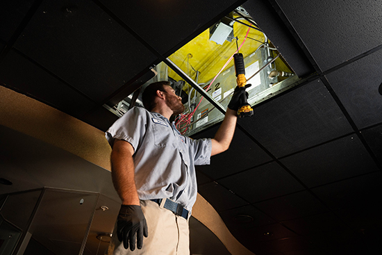 commercial ac installation final checks, man on ladder looking into ceiling ac unit